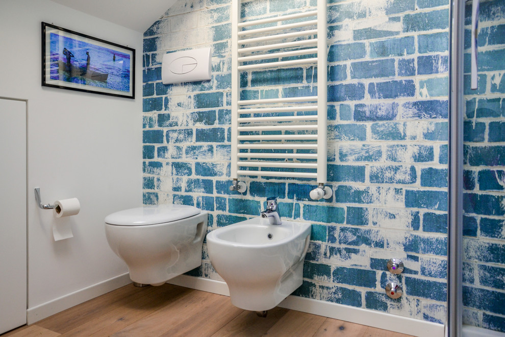 This is an example of a small contemporary 3/4 bathroom in Milan with flat-panel cabinets, light wood cabinets, a corner shower, a wall-mount toilet, blue walls, light hardwood floors, a vessel sink and laminate benchtops.