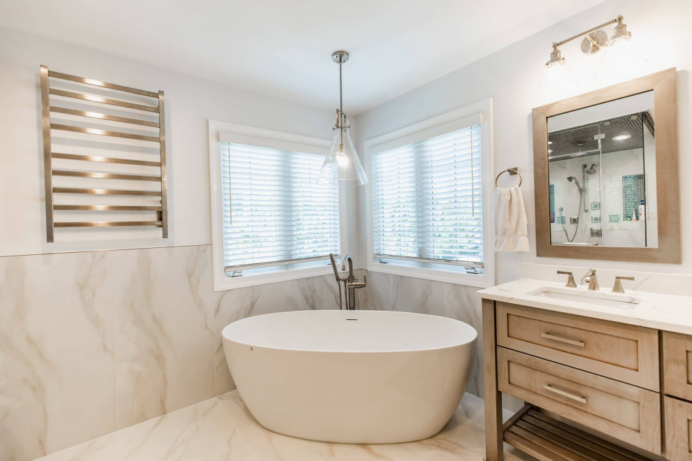 This is an example of a large contemporary master bathroom in Baltimore with a freestanding tub, a one-piece toilet, gray tile, grey walls, a drop-in sink, marble benchtops, beige benchtops, a shower seat, a double vanity and a built-in vanity.