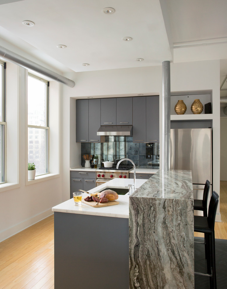 Photo of a small contemporary galley open plan kitchen in Boston with an undermount sink, flat-panel cabinets, grey cabinets, granite benchtops, metallic splashback, mirror splashback, stainless steel appliances, light hardwood floors and with island.