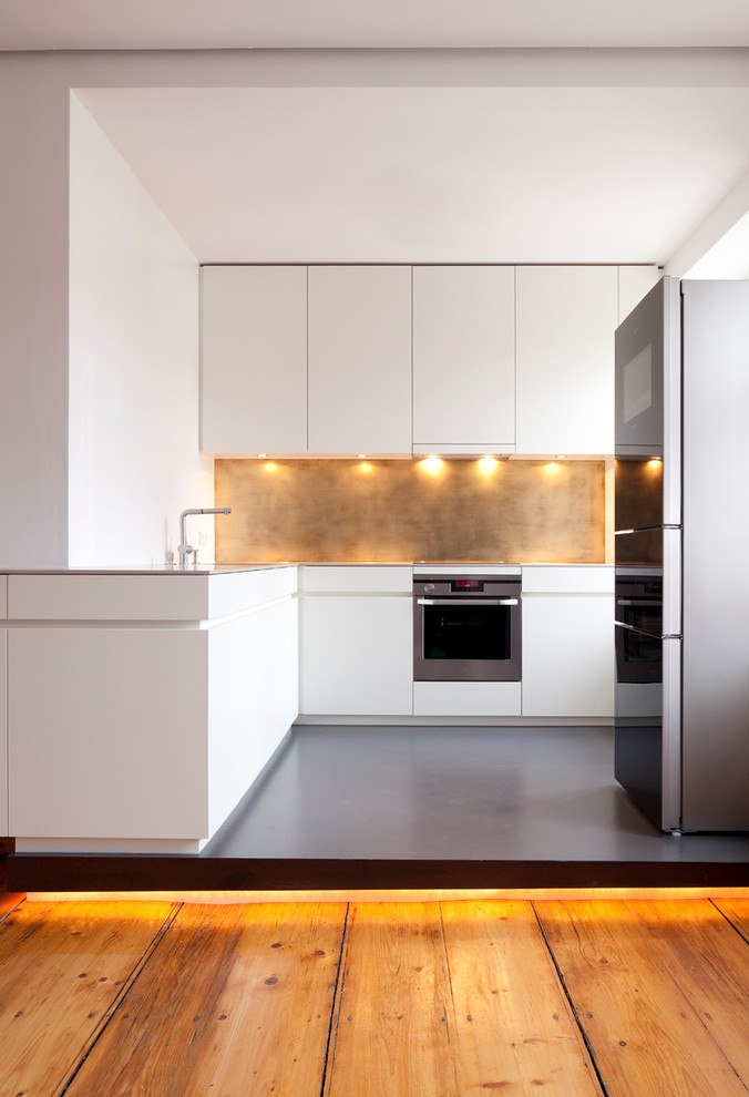 Mid-sized contemporary l-shaped separate kitchen in Munich with flat-panel cabinets, white cabinets, solid surface benchtops, metallic splashback, stainless steel appliances and linoleum floors.