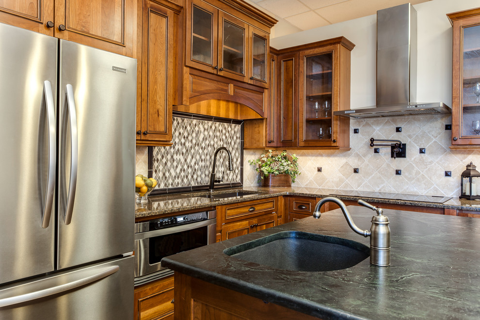 This is an example of a small traditional kitchen in Denver with a drop-in sink, recessed-panel cabinets, medium wood cabinets, granite benchtops, beige splashback, mosaic tile splashback, stainless steel appliances, travertine floors and with island.