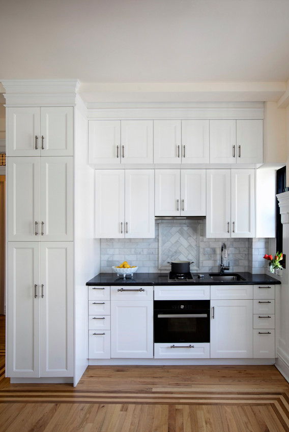 Exempel på ett mellanstort modernt svart linjärt svart kök och matrum, med en enkel diskho, luckor med upphöjd panel, vita skåp, bänkskiva i kvartsit, grått stänkskydd, stänkskydd i stenkakel, målat trägolv och brunt golv