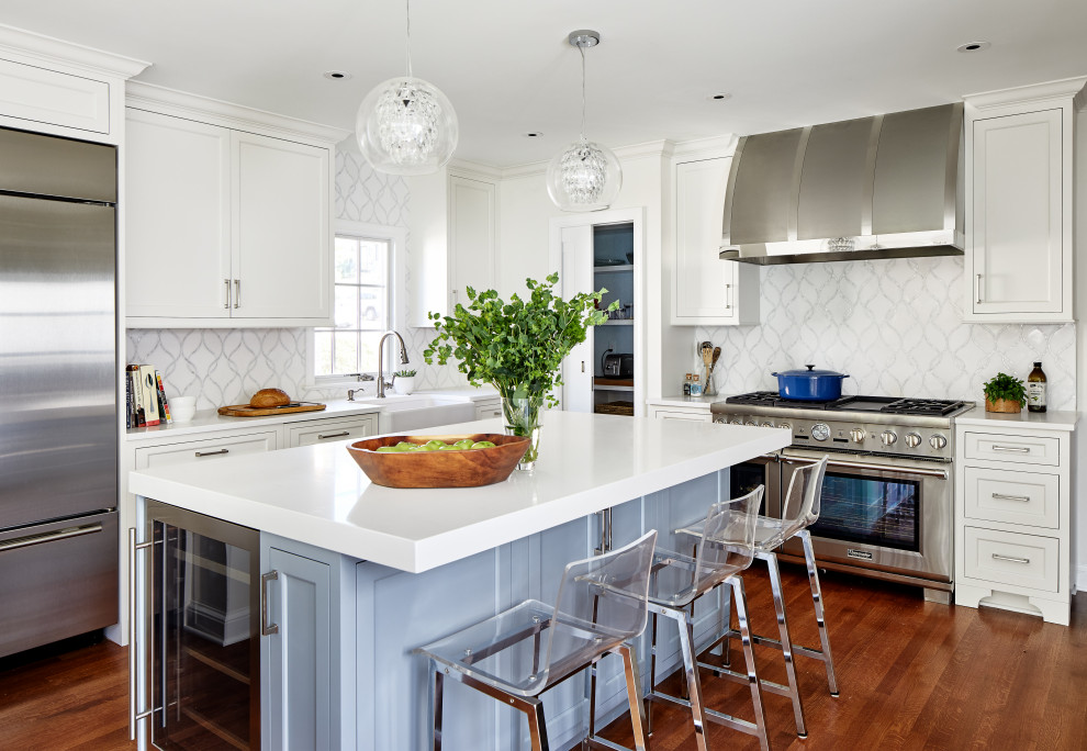 This is an example of a mid-sized transitional u-shaped eat-in kitchen in DC Metro with a farmhouse sink, recessed-panel cabinets, blue cabinets, quartz benchtops, white splashback, marble splashback, panelled appliances, medium hardwood floors, with island, brown floor and white benchtop.