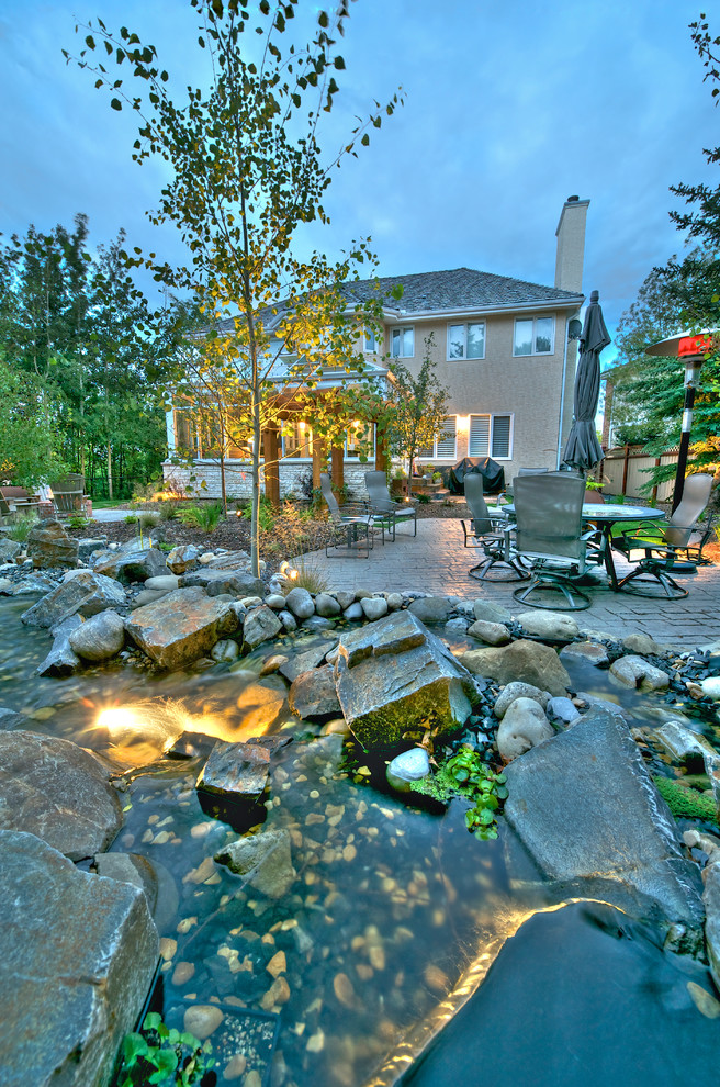 This is an example of a mid-sized traditional backyard patio in Calgary with a water feature and no cover.