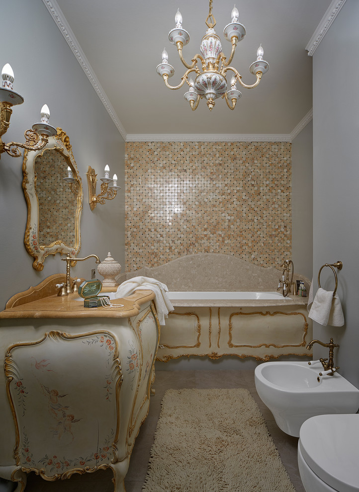 Inspiration for a small traditional master bathroom in Yekaterinburg with an undermount tub, a wall-mount toilet, beige tile, grey walls, porcelain floors, an undermount sink, limestone benchtops, beige cabinets and flat-panel cabinets.