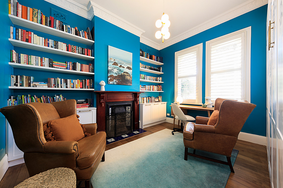 На фото: маленькая гостевая спальня (комната для гостей) в стиле неоклассика (современная классика) с синими стенами, паркетным полом среднего тона, стандартным камином, фасадом камина из дерева и коричневым полом для на участке и в саду