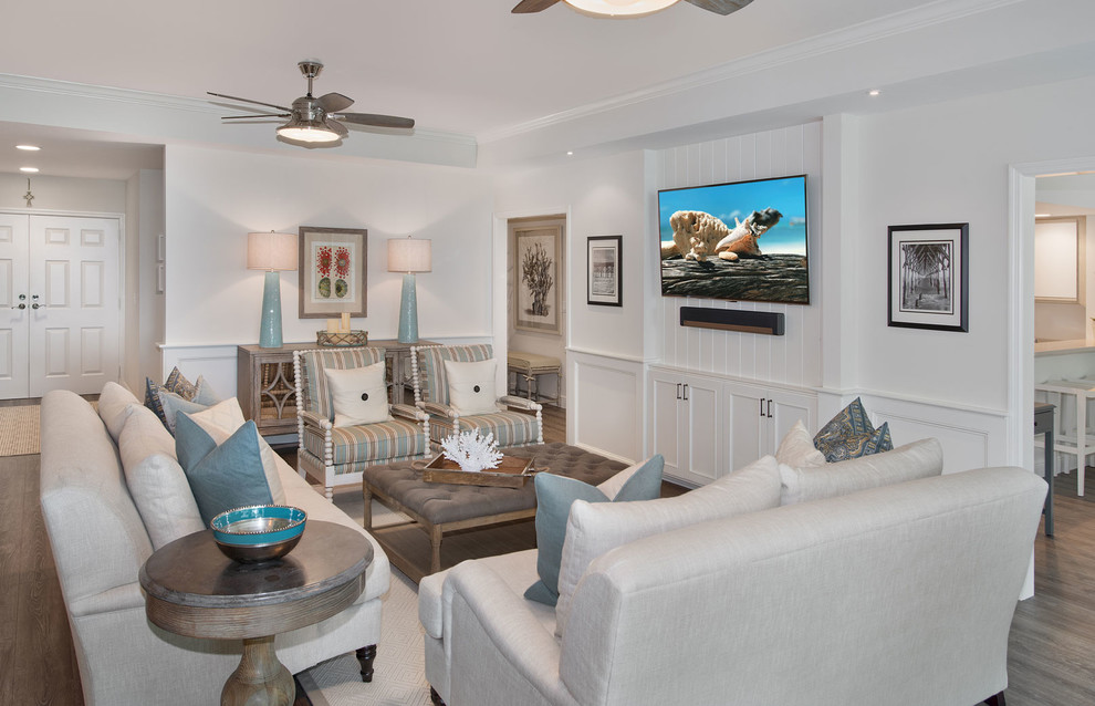 Photo of a mid-sized beach style formal enclosed living room with white walls, medium hardwood floors, a wall-mounted tv, no fireplace and brown floor.