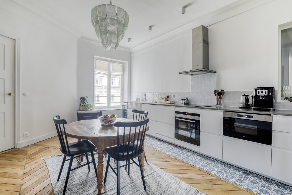 Photo of a mid-sized contemporary single-wall open plan kitchen in Paris with an undermount sink, beaded inset cabinets, white cabinets, quartzite benchtops, white splashback, subway tile splashback, stainless steel appliances, light hardwood floors, no island, brown floor and grey benchtop.