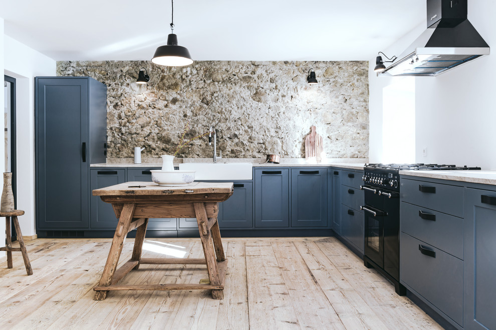 This is an example of an expansive country l-shaped kitchen in Munich with a farmhouse sink, shaker cabinets, blue cabinets, black appliances, light hardwood floors, with island, beige floor and beige benchtop.