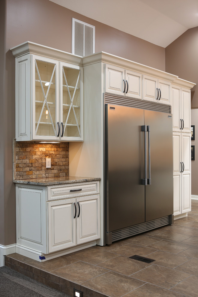 Open concept kitchen - large transitional u-shaped porcelain tile and brown floor open concept kitchen idea with a farmhouse sink, raised-panel cabinets, white cabinets, granite countertops, beige backsplash, travertine backsplash, stainless steel appliances and an island