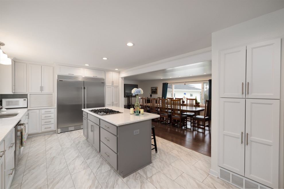 Large transitional l-shaped ceramic tile and white floor enclosed kitchen photo with an undermount sink, shaker cabinets, white cabinets, quartz countertops, white backsplash, subway tile backsplash, stainless steel appliances, an island and white countertops