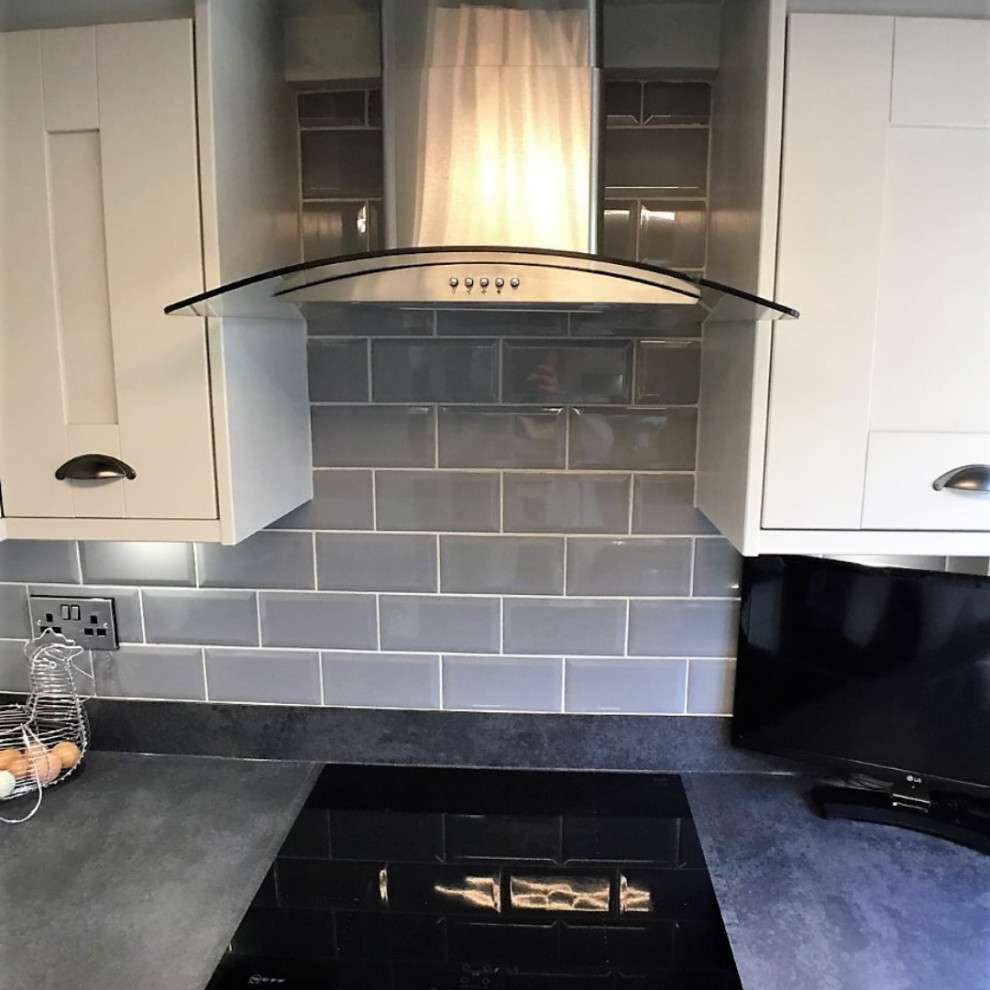 Mid-sized traditional galley kitchen in Other with shaker cabinets, grey cabinets, laminate benchtops, grey splashback, porcelain splashback, black appliances, brown floor and grey benchtop.
