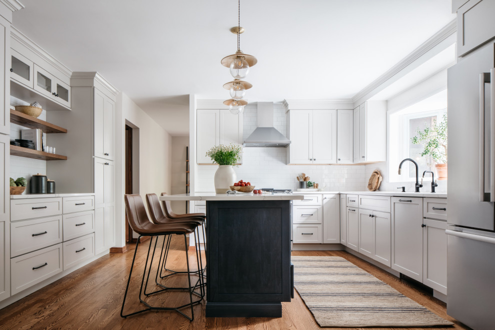 Example of a transitional medium tone wood floor kitchen design in Chicago with white cabinets, white backsplash, subway tile backsplash, stainless steel appliances, an island and white countertops