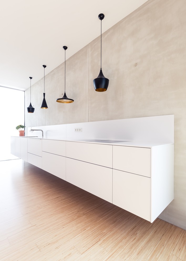 Inspiration for a mid-sized modern single-wall open plan kitchen in Frankfurt with white cabinets, white splashback, no island, white benchtop and bamboo floors.