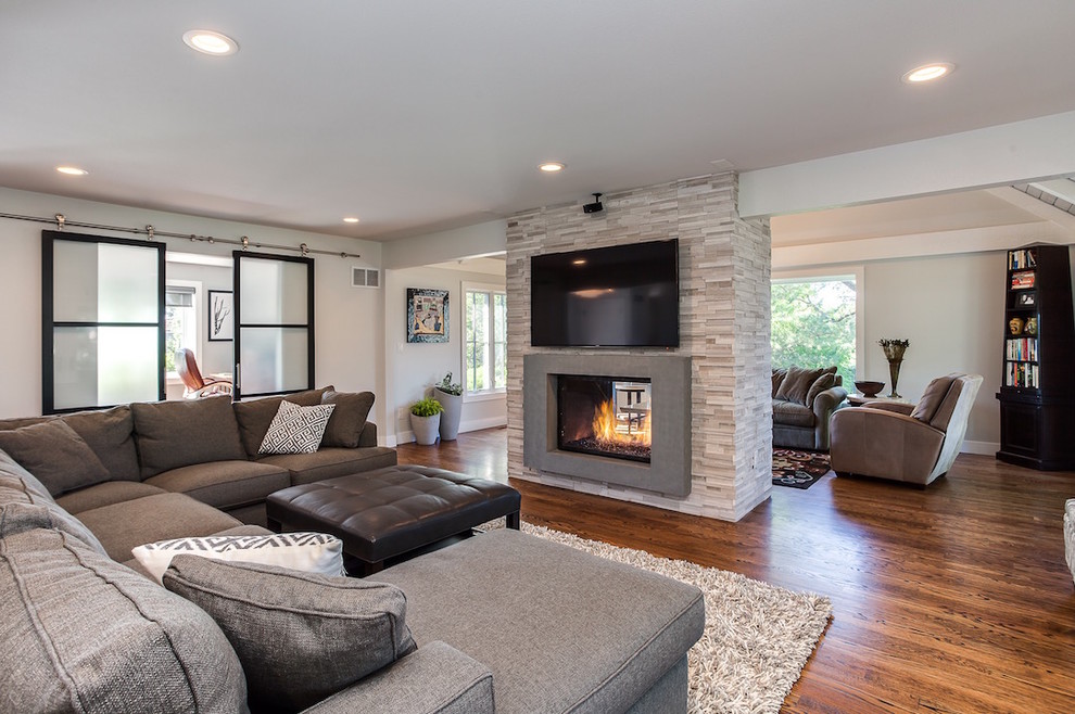 Photo of a large contemporary open concept family room in Denver with a library, grey walls, medium hardwood floors, a two-sided fireplace, a concrete fireplace surround and no tv.