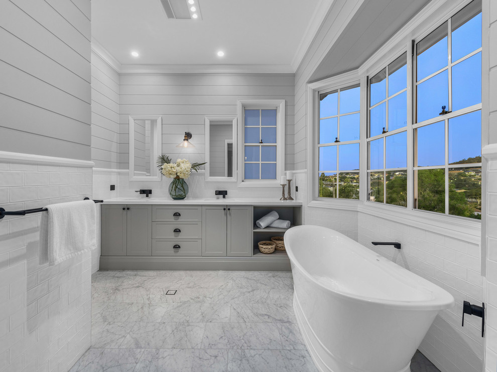 This is an example of a beach style master bathroom in Brisbane with shaker cabinets, grey cabinets, a freestanding tub, white tile, subway tile, grey walls, grey floor and white benchtops.
