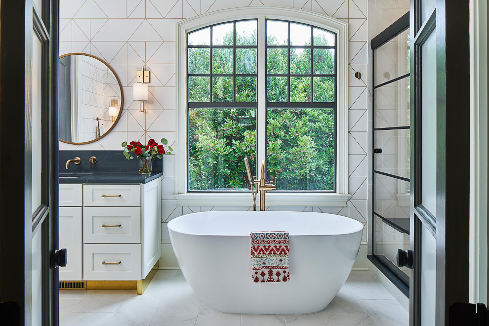 Inspiration for a mid-sized transitional master bathroom in Charlotte with shaker cabinets, white cabinets, a freestanding tub, an alcove shower, a two-piece toilet, white tile, porcelain tile, white walls, porcelain floors, an undermount sink, engineered quartz benchtops, white floor, a sliding shower screen and black benchtops.