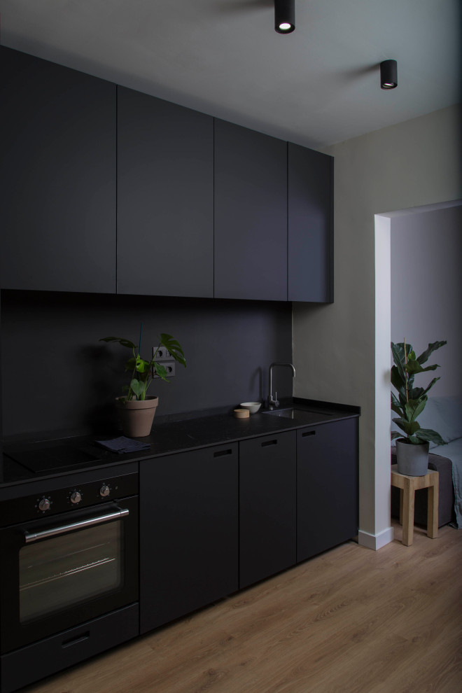 Inredning av ett avskilt, litet svart svart parallellkök, med en integrerad diskho, skåp i shakerstil, svarta skåp, bänkskiva i kvartsit, svart stänkskydd, stänkskydd i keramik, svarta vitvaror, plywoodgolv och brunt golv
