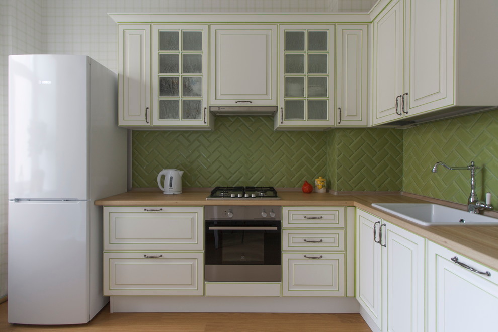 Пример оригинального дизайна: отдельная, угловая кухня с фасадами с выступающей филенкой, белыми фасадами, зеленым фартуком и фартуком из керамической плитки без острова