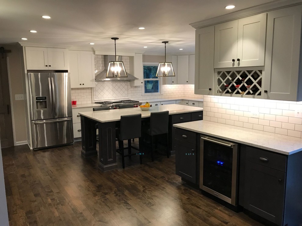 Large transitional u-shaped kitchen in Chicago with an undermount sink, shaker cabinets, white cabinets, quartzite benchtops, white splashback, subway tile splashback, stainless steel appliances, dark hardwood floors, with island and brown floor.