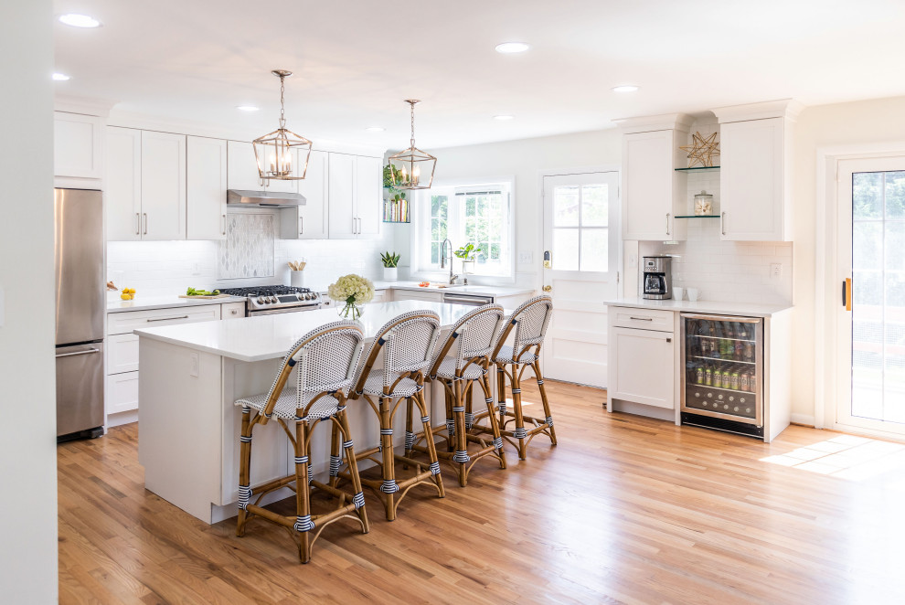 Mid-sized transitional l-shaped light wood floor and brown floor eat-in kitchen photo in Baltimore with an undermount sink, shaker cabinets, white cabinets, quartz countertops, white backsplash, marble backsplash, stainless steel appliances, an island and white countertops