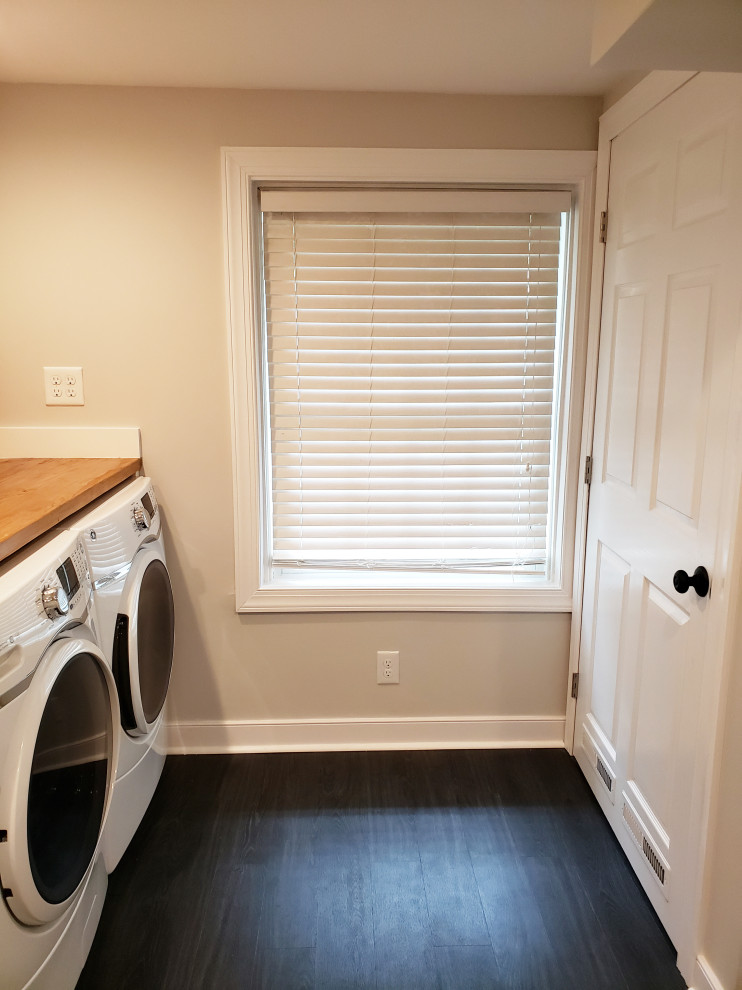 Large traditional single-wall utility room in Richmond with a single-bowl sink, raised-panel cabinets, white cabinets, wood benchtops, grey walls, vinyl floors, a side-by-side washer and dryer, black floor and brown benchtop.