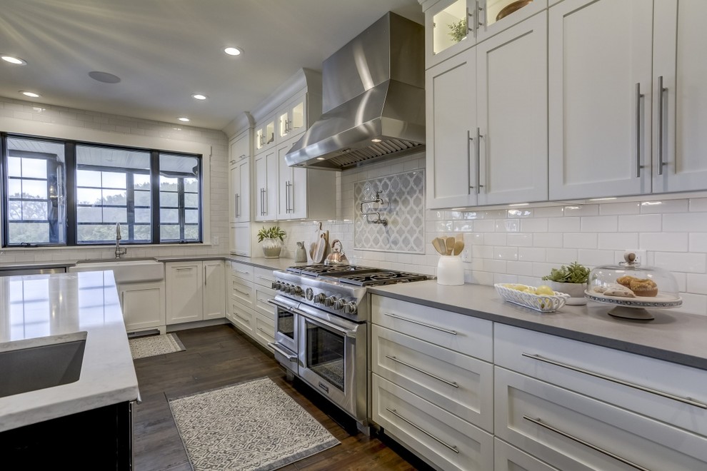 This is an example of a large country u-shaped open plan kitchen in Chicago with a farmhouse sink, recessed-panel cabinets, white cabinets, quartz benchtops, white splashback, subway tile splashback, stainless steel appliances, porcelain floors, with island, brown floor and white benchtop.