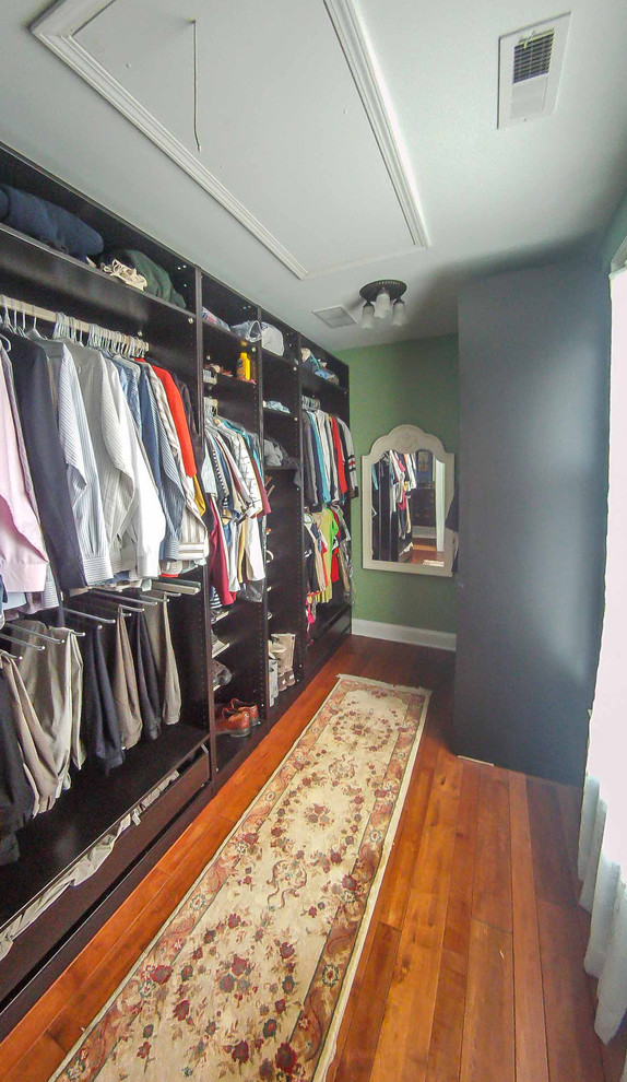 Large traditional gender-neutral walk-in wardrobe in Chicago with raised-panel cabinets, dark wood cabinets, medium hardwood floors, brown floor and wallpaper.