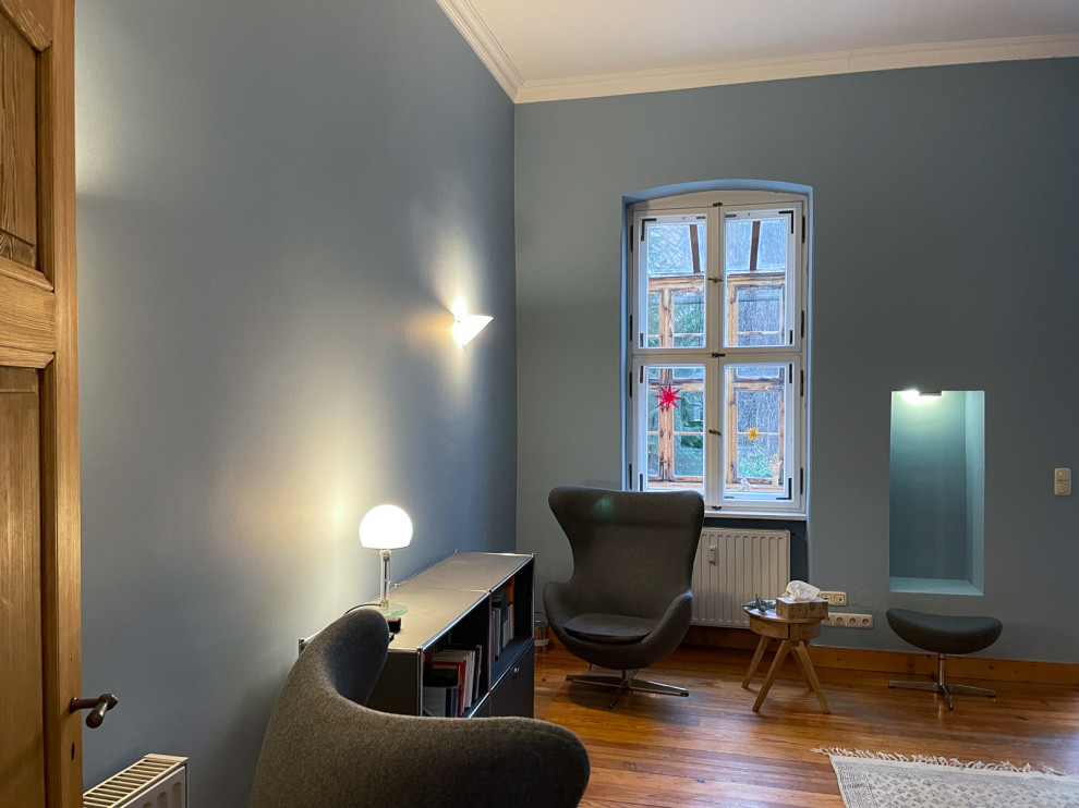Mittelgroßes Skandinavisches Arbeitszimmer mit blauer Wandfarbe, braunem Holzboden, freistehendem Schreibtisch und braunem Boden in Berlin