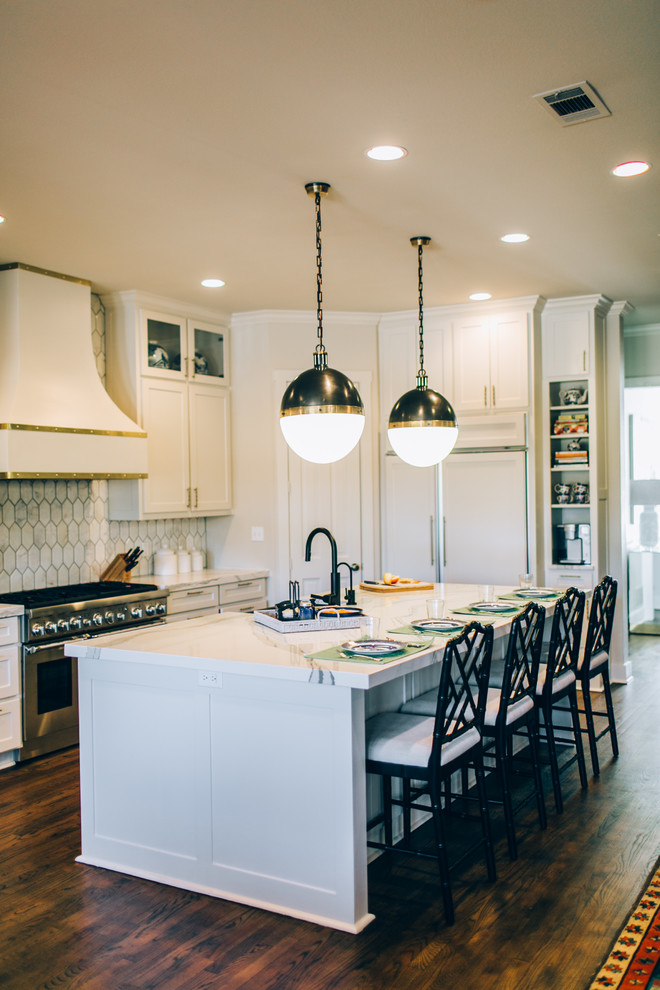 Design ideas for a mid-sized transitional l-shaped open plan kitchen in Dallas with a farmhouse sink, shaker cabinets, white cabinets, quartz benchtops, white splashback, stainless steel appliances, medium hardwood floors, with island, marble splashback and brown floor.