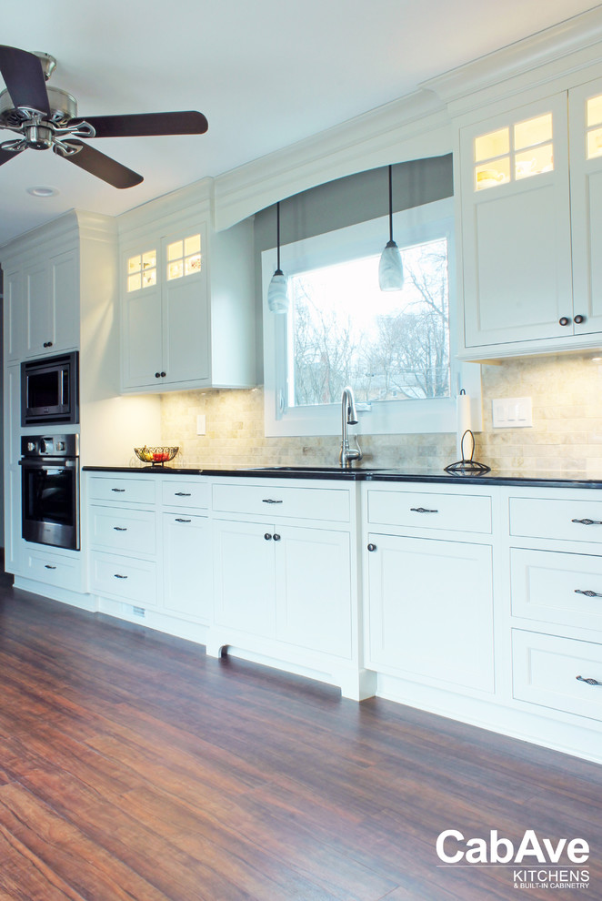 Example of a mid-sized transitional l-shaped vinyl floor and brown floor eat-in kitchen design with an undermount sink, recessed-panel cabinets, white cabinets, quartz countertops, beige backsplash, ceramic backsplash, stainless steel appliances and no island
