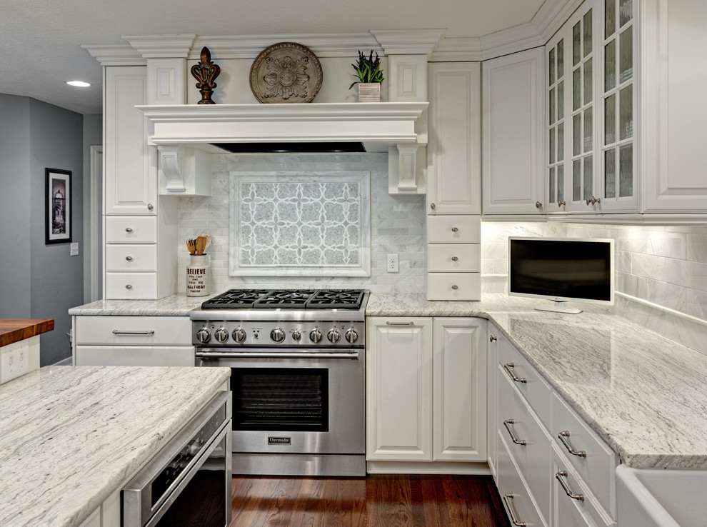 Large traditional u-shaped eat-in kitchen in Minneapolis with a farmhouse sink, raised-panel cabinets, white cabinets, granite benchtops, panelled appliances, dark hardwood floors, multiple islands, white splashback, marble splashback, white benchtop and brown floor.