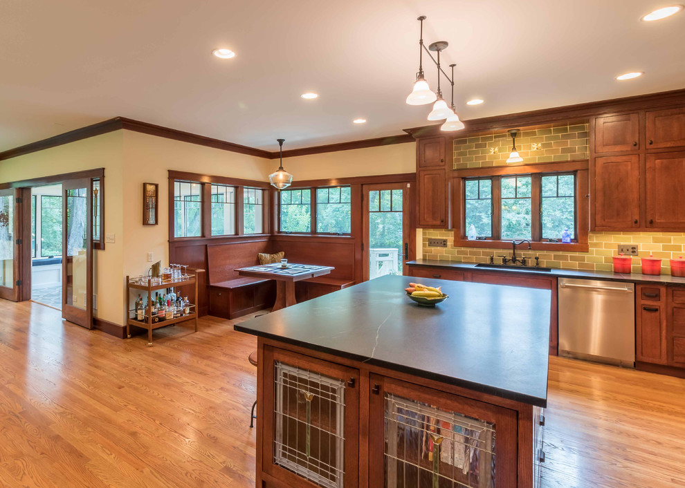 Mid-sized arts and crafts l-shaped open plan kitchen in Chicago with an undermount sink, shaker cabinets, medium wood cabinets, soapstone benchtops, green splashback, ceramic splashback, stainless steel appliances, light hardwood floors, with island, black benchtop, brown floor and wallpaper.