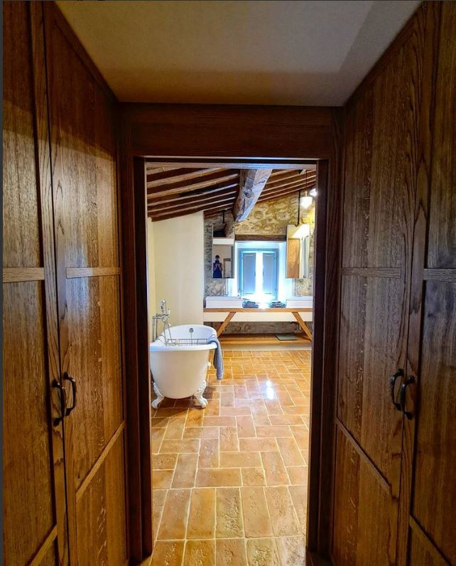 Пример оригинального дизайна: большая главная ванная комната в классическом стиле с открытыми фасадами, бежевыми фасадами, ванной на ножках, душем без бортиков, раздельным унитазом, бежевой плиткой, плиткой из известняка, бежевыми стенами, кирпичным полом, настольной раковиной, столешницей из дерева, коричневым полом, душем с распашными дверями, коричневой столешницей, тумбой под две раковины, встроенной тумбой, балками на потолке и кирпичными стенами