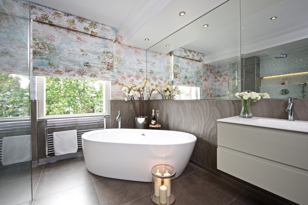 Photo of a large contemporary bathroom in London with an integrated sink, flat-panel cabinets, grey cabinets, a freestanding tub, a curbless shower, a one-piece toilet, gray tile, ceramic tile and solid surface benchtops.