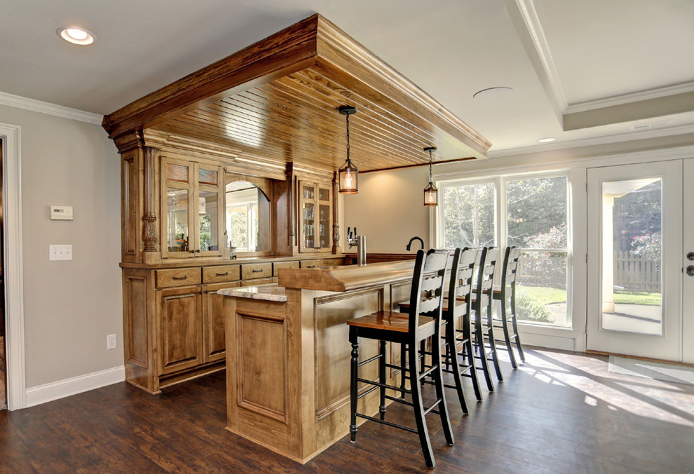 This is an example of a mid-sized traditional l-shaped seated home bar in Atlanta with an undermount sink, raised-panel cabinets, brown cabinets, granite benchtops, mirror splashback, vinyl floors and brown floor.