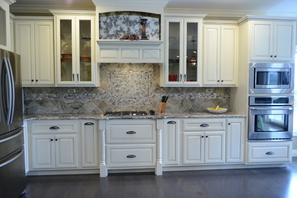Example of a huge transitional l-shaped medium tone wood floor eat-in kitchen design in Chicago with a farmhouse sink, raised-panel cabinets, white cabinets, granite countertops, beige backsplash, stone tile backsplash, stainless steel appliances and an island