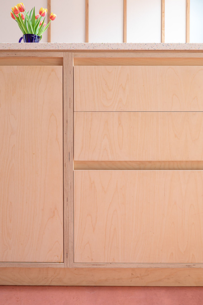 Modelo de cocina contemporánea grande abierta con armarios con paneles lisos, puertas de armario de madera clara, suelo de cemento, una isla y suelo rosa