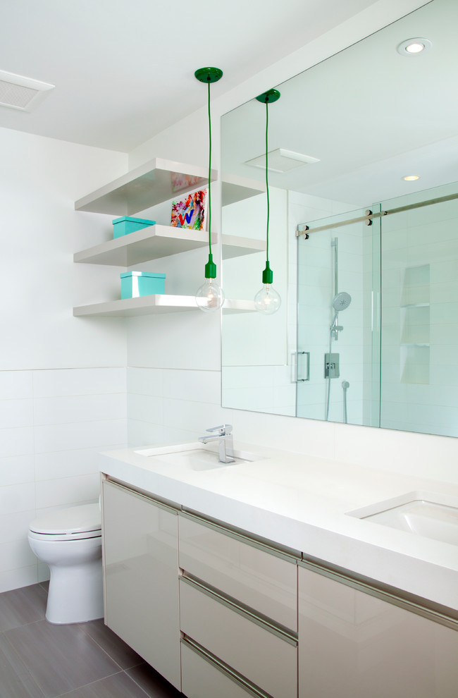 Inspiration for a mid-sized contemporary kids bathroom in Calgary with flat-panel cabinets, white cabinets, engineered quartz benchtops, white tile, ceramic tile, an undermount sink, white walls, ceramic floors, an alcove shower, grey floor and a sliding shower screen.