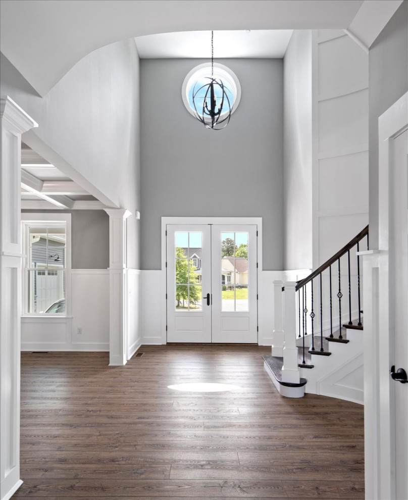 Example of a huge beach style vinyl floor, multicolored floor, coffered ceiling and wainscoting entryway design in Other with multicolored walls and a white front door
