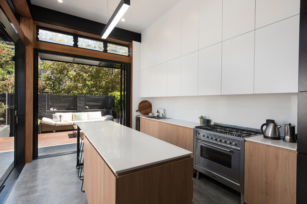 This is an example of a mid-sized modern single-wall eat-in kitchen in Newcastle - Maitland with a double-bowl sink, flat-panel cabinets, white cabinets, white splashback, stainless steel appliances, concrete floors, grey floor and white benchtop.