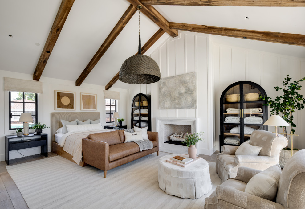 Klassisches Hauptschlafzimmer mit weißer Wandfarbe, braunem Holzboden, Kamin, Kaminumrandung aus Stein, braunem Boden, freigelegten Dachbalken, gewölbter Decke und Wandpaneelen in Orange County