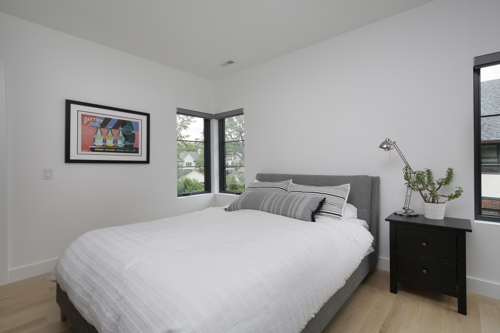 Large modern guest bedroom in Chicago with white walls and light hardwood floors.