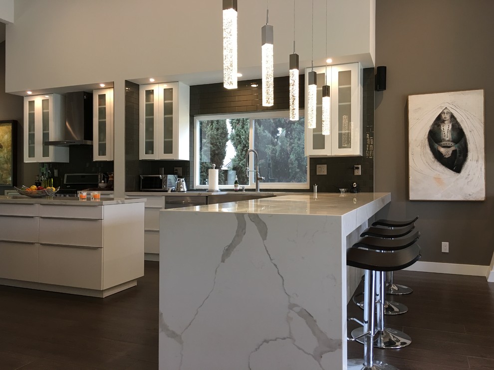 Mid-sized modern single-wall separate kitchen in Orange County with a farmhouse sink, glass-front cabinets, white cabinets, marble benchtops, grey splashback, glass tile splashback, stainless steel appliances, medium hardwood floors, with island and grey floor.