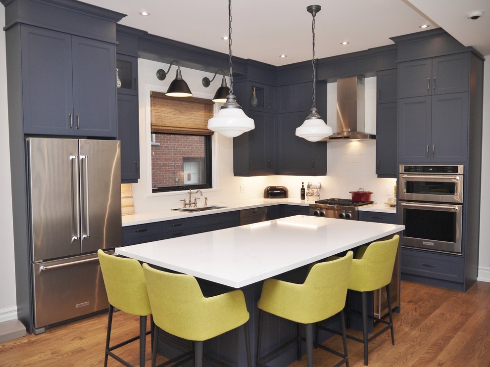 Inspiration for a mid-sized transitional l-shaped eat-in kitchen in Toronto with an undermount sink, shaker cabinets, blue cabinets, quartz benchtops, white splashback, porcelain splashback, stainless steel appliances, medium hardwood floors, with island, brown floor and white benchtop.