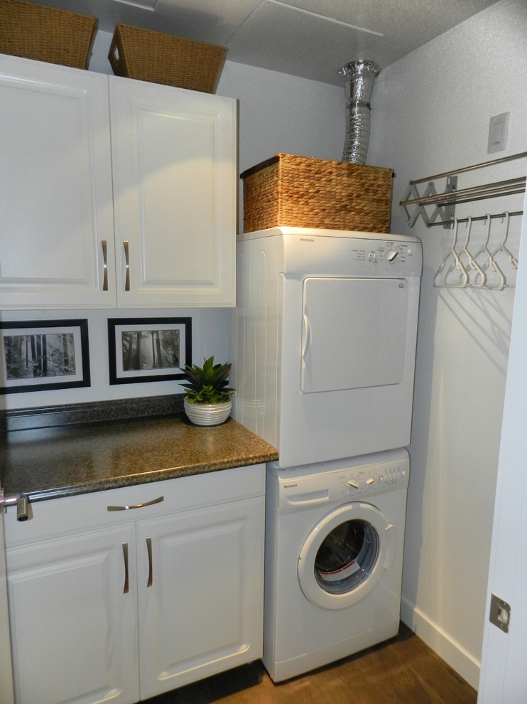 Design ideas for a small transitional single-wall laundry cupboard in Vancouver with laminate benchtops, white walls, medium hardwood floors, a stacked washer and dryer, grey floor, raised-panel cabinets and white cabinets.