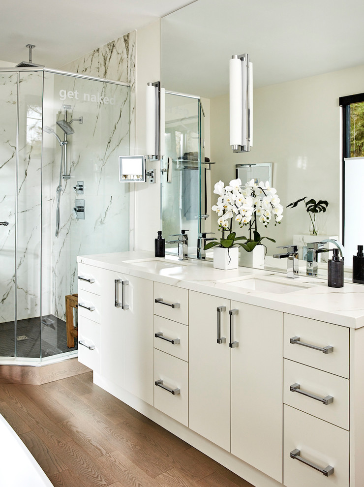 Mid-sized contemporary master bathroom in Montreal with flat-panel cabinets, white cabinets, a freestanding tub, a corner shower, a one-piece toilet, white tile, marble, white walls, medium hardwood floors, an undermount sink, marble benchtops, grey floor, a sliding shower screen and white benchtops.
