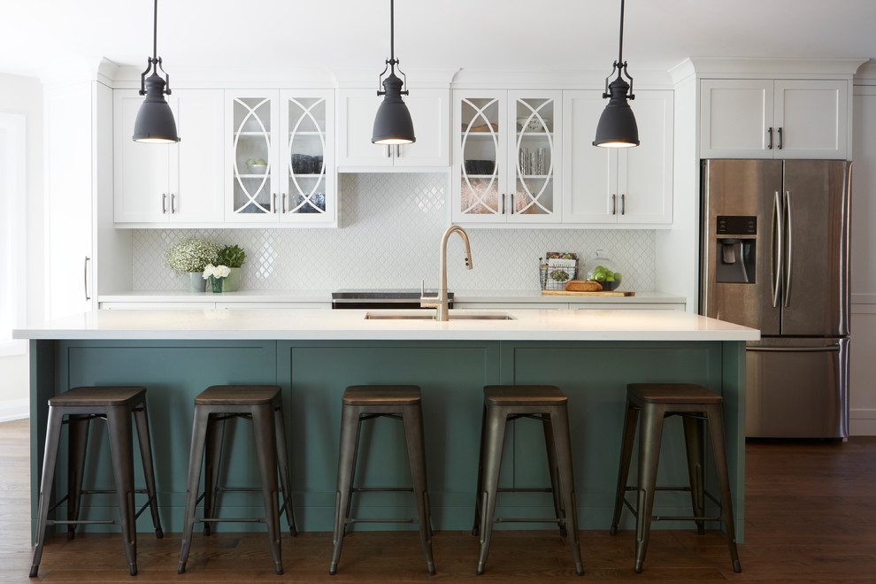 Inspiration for a large transitional single-wall eat-in kitchen in Toronto with a drop-in sink, glass-front cabinets, green cabinets, quartz benchtops, white splashback, ceramic splashback, stainless steel appliances, medium hardwood floors, with island, brown floor and white benchtop.