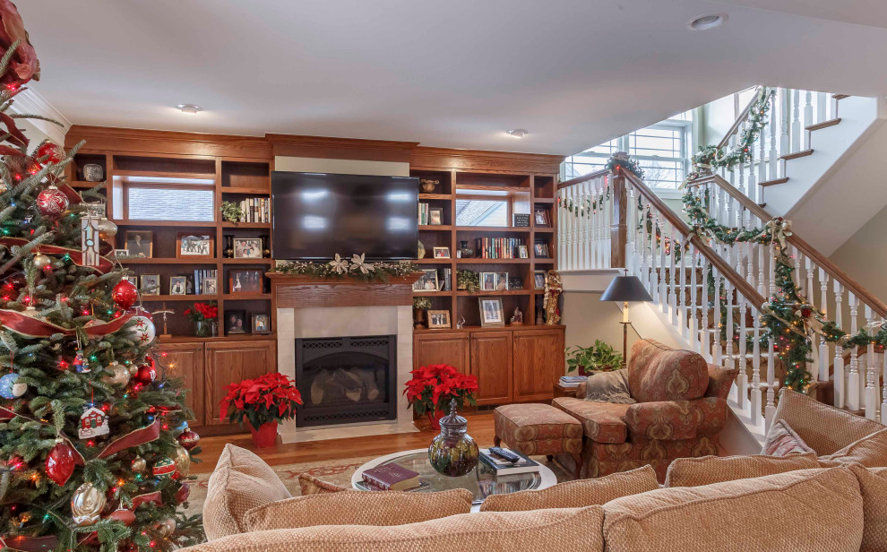 This is an example of a mid-sized arts and crafts formal open concept living room in Detroit with beige walls, medium hardwood floors, a standard fireplace, a wood fireplace surround, a wall-mounted tv, brown floor, wallpaper and wallpaper.