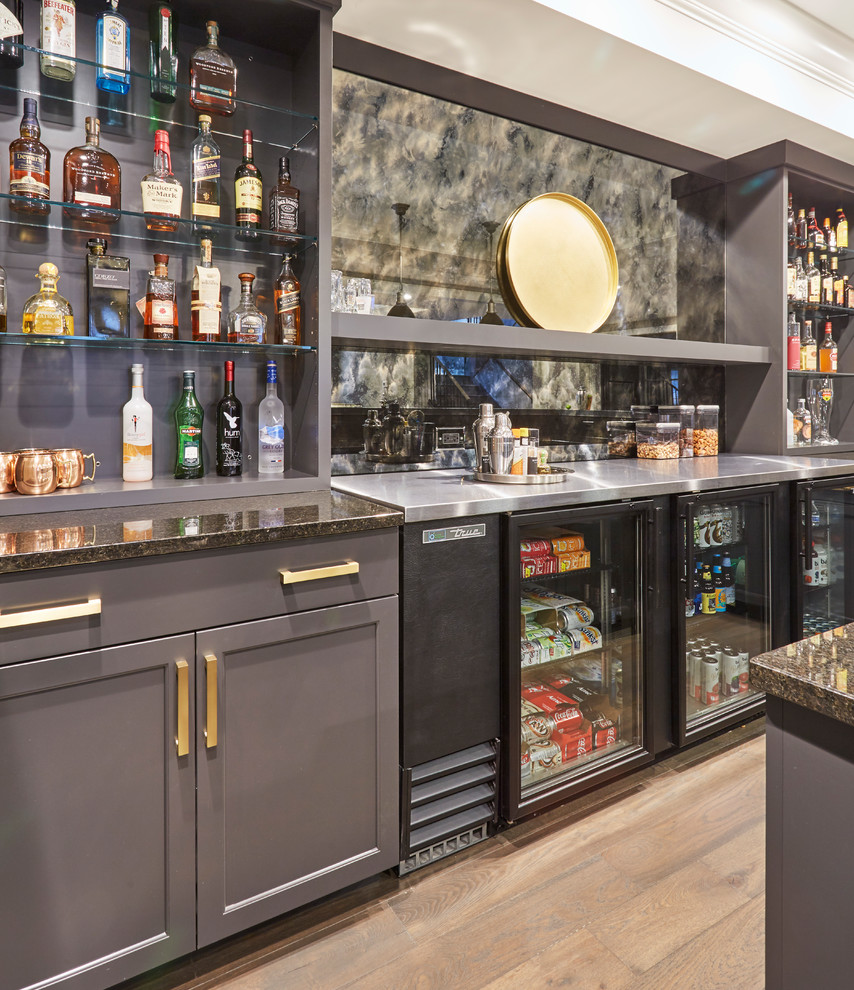 This is an example of a large transitional u-shaped seated home bar in Chicago with an undermount sink, shaker cabinets, grey cabinets, concrete benchtops, multi-coloured splashback, glass sheet splashback, light hardwood floors, multi-coloured floor and beige benchtop.
